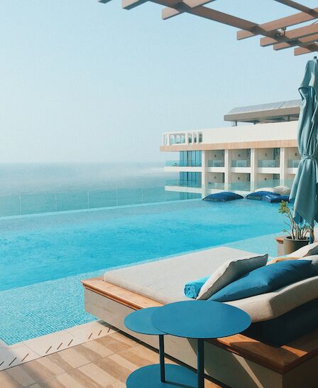 A luxurious poolside setup with lounge chairs, umbrellas, and a stunning ocean view, adjacent to a modern resort building.