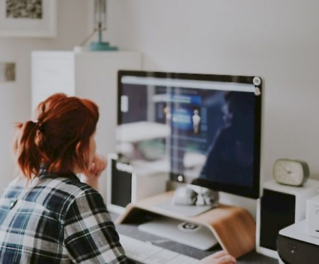 A person wearing a plaid shirt is working at a desk with a computer, in a room with minimalist decor and various items on the desk.