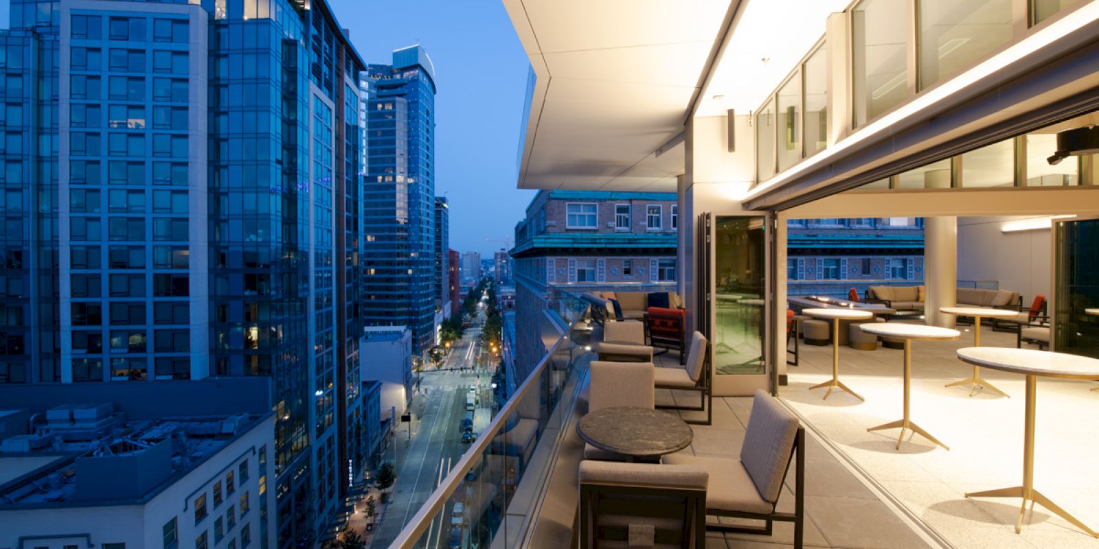This image shows an outdoor terrace with seating areas, overlooking a cityscape with high-rise buildings. The terrace features tables and chairs.