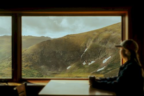 A person is sitting at a table with a scenic mountainous view visible through a window. The person appears to be enjoying the landscape.