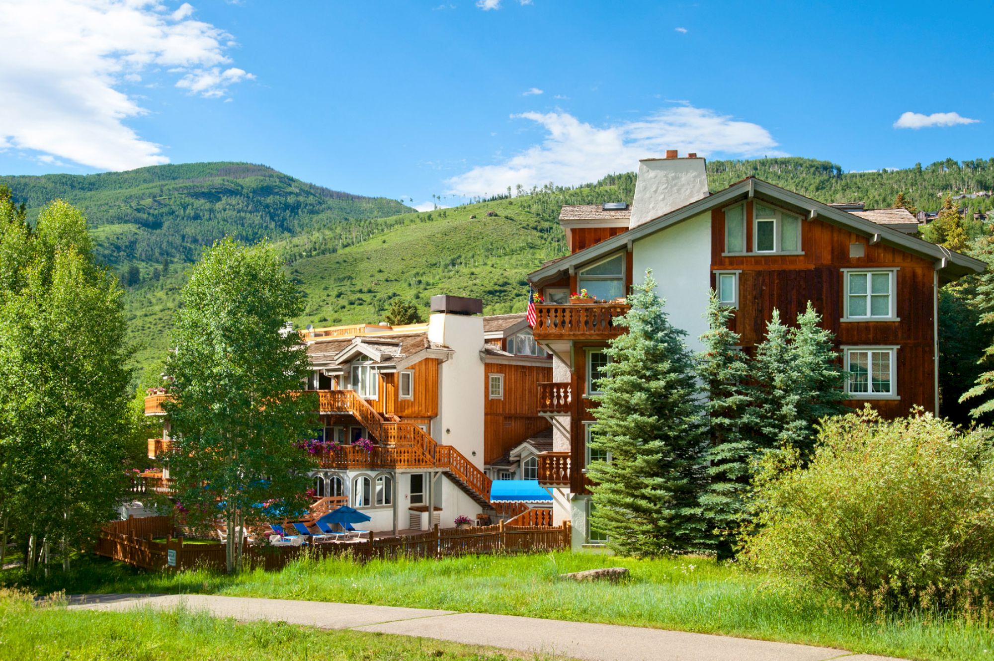 A charming, chalet-style building surrounded by lush greenery, with mountainous scenery in the background and clear blue sky above, completing the view.