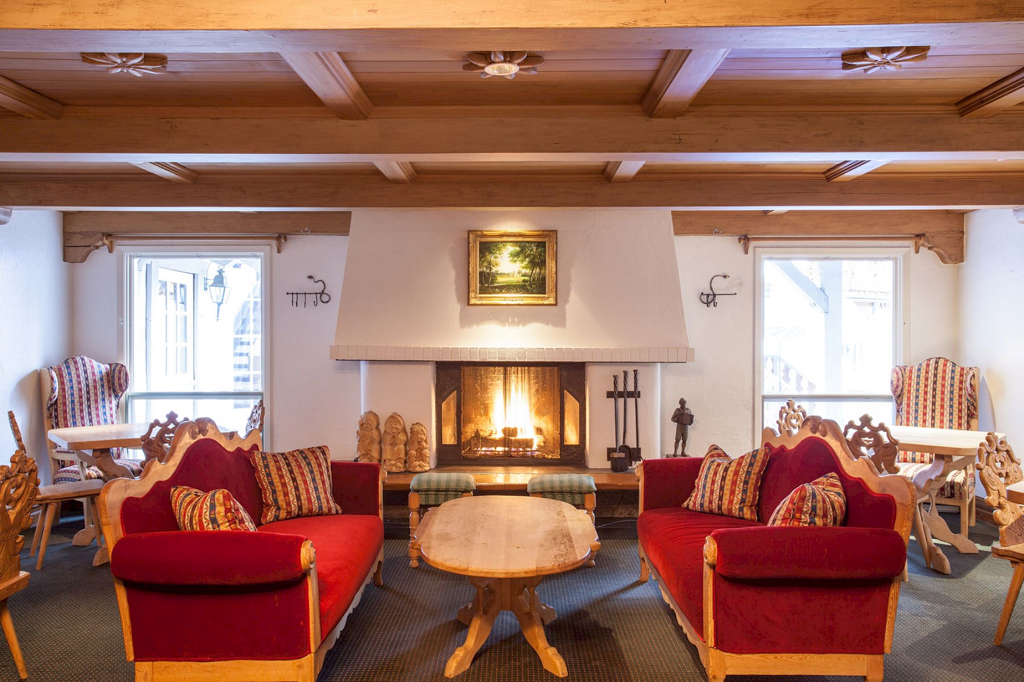 This is a cozy room with wooden furniture, red upholstered sofas, a fireplace, and a painting above it, creating a warm, inviting atmosphere.