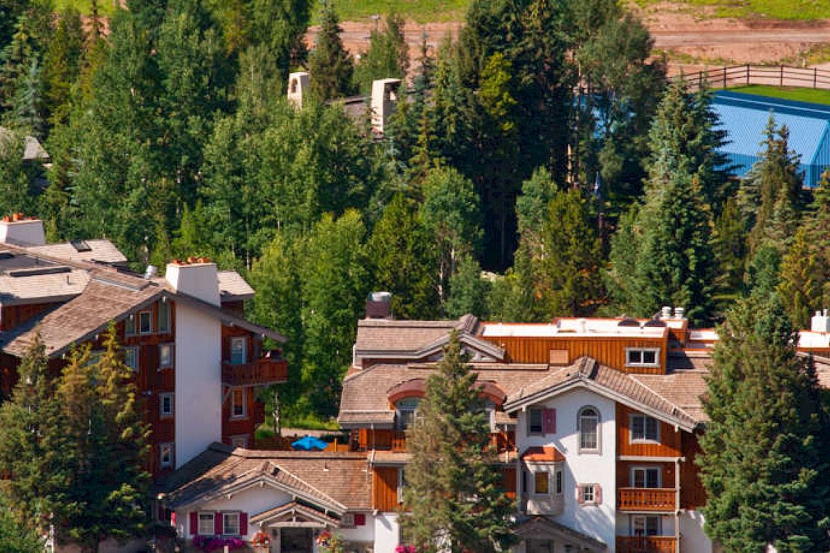 The image shows a scenic view of a residential area with houses nestled among trees, with a pool and pathways visible in the background.