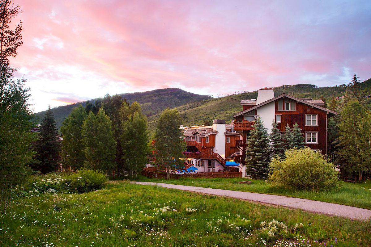 Scenic view of a lodge surrounded by trees, with a mountain in the background and a vibrant sunset sky.
