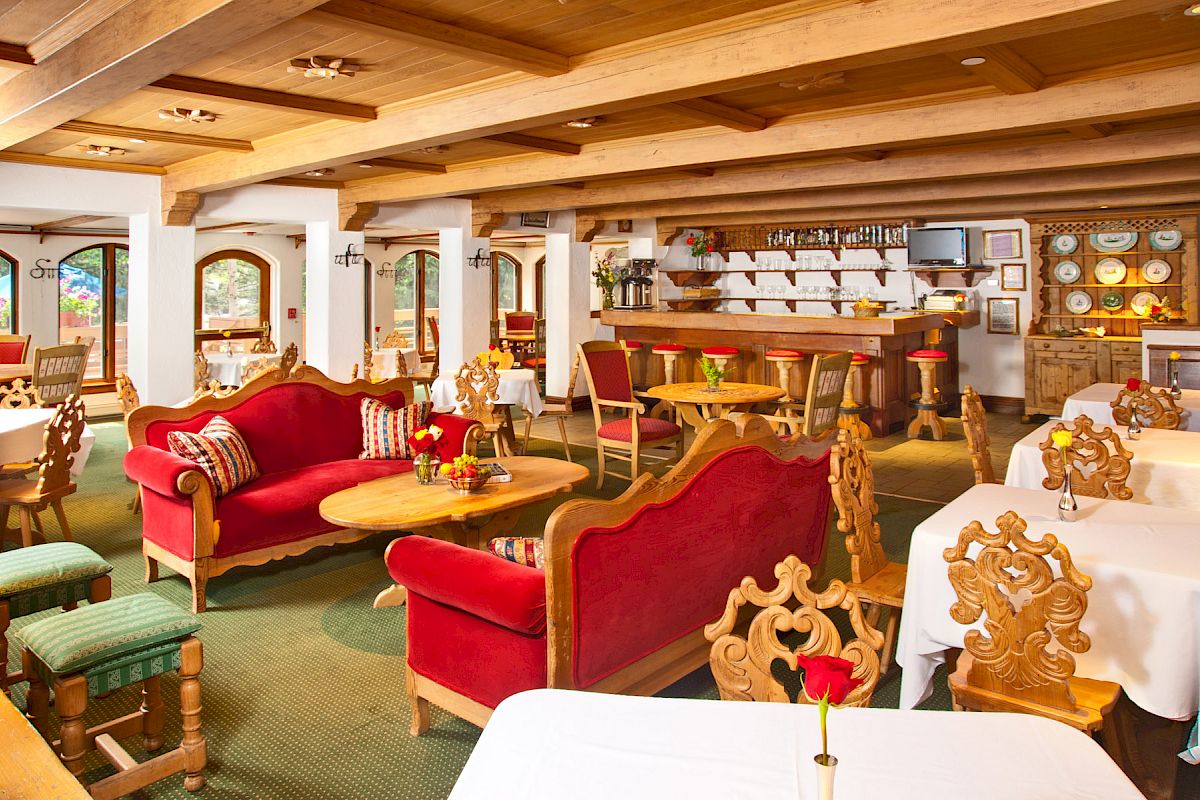 A cozy, rustic restaurant interior with red sofas, wooden furniture, a bar area, and tables set with white tablecloths and flowers.