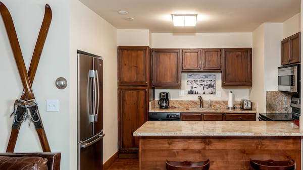 A cozy kitchen with wood cabinets, a granite countertop, two stools, vintage skis on the wall, and stainless steel appliances.