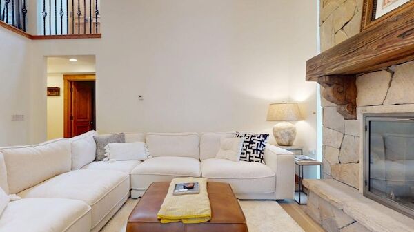 The image shows a cozy living room with a sectional sofa, a coffee table, a stone fireplace, and warm lighting.