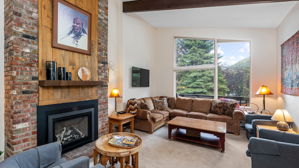A cozy living room with a fireplace, large window, and seating area featuring a sectional sofa and two armchairs.