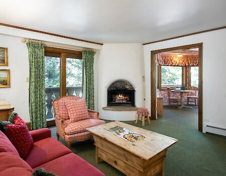 Cozy living room with red sofa, pink chairs, wooden coffee table, stone fireplace, green carpet, and windows with green curtains, a warm homey vibe.