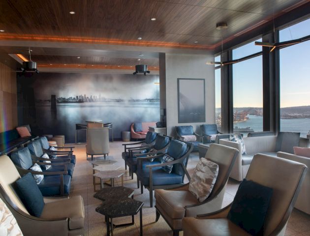 A stylish lounge with various seating, a cityscape mural on one wall, and large windows offering a scenic view of water and a Ferris wheel, ending the sentence.