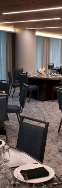 A banquet hall set for an event with round tables, chairs, plates, glasses, utensils, and floral centerpieces under a ceiling with recessed lighting.