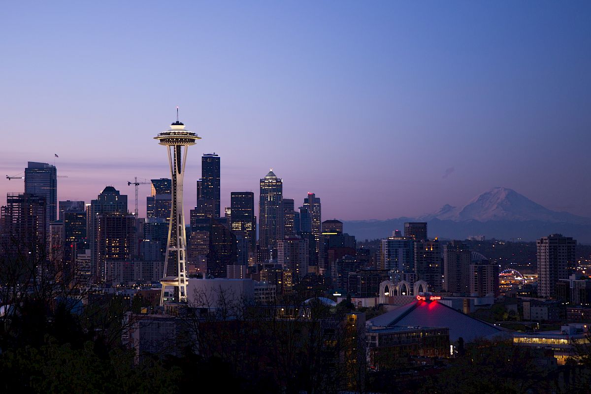 The image shows Seattle's skyline at dusk, with the Space Needle prominently featured and Mount Rainier visible in the background.
