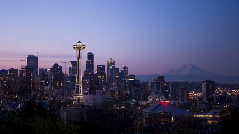 The image shows Seattle's skyline at dusk, with the Space Needle prominently featured and Mount Rainier visible in the background.